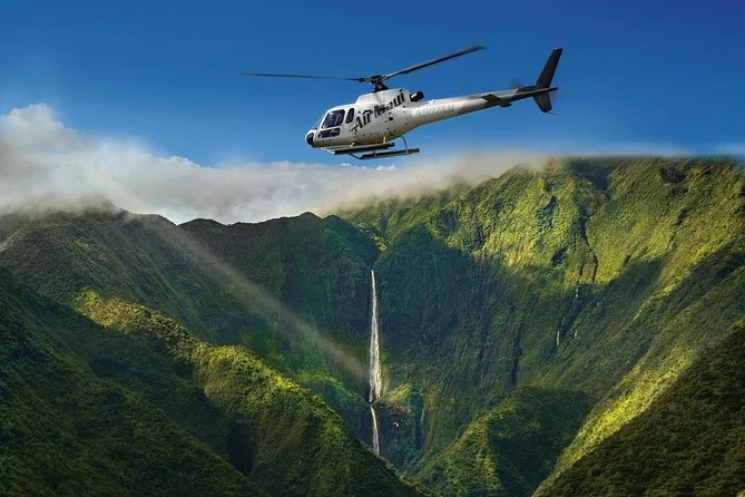 A helicopter above a green valley with a tall waterfall