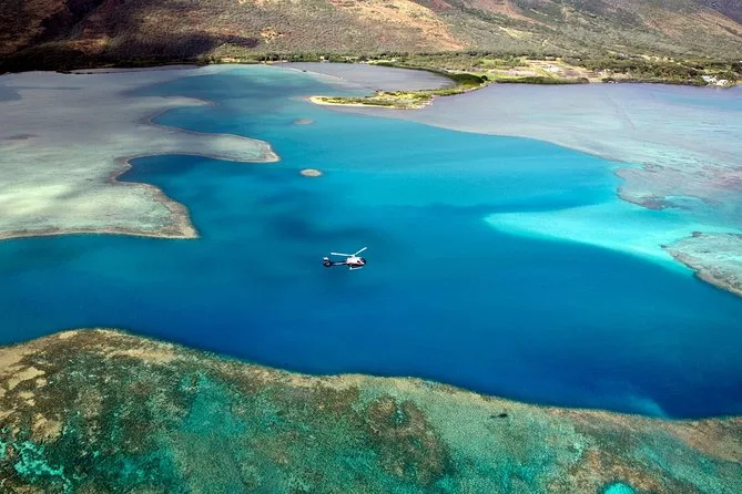 Un helicóptero cruzando una laguna de arrecife turquesa bajo una costa seca