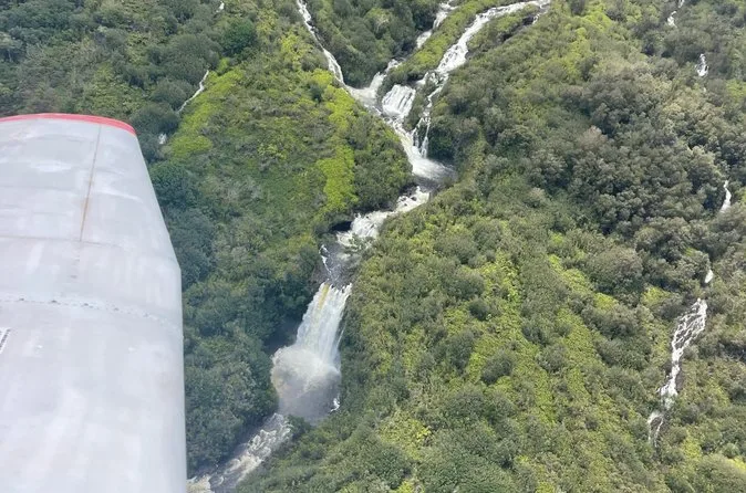 A small plane's wing above a waterfall cascading through green forest