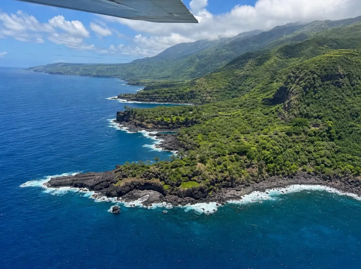 A green volcanic coastline seen from under a small plane's wing
